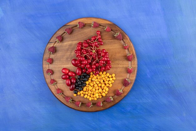 A wooden board full of berries on blue surface