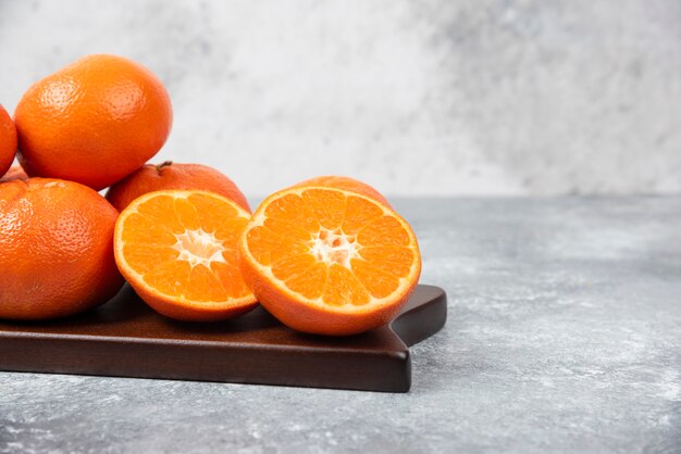 A wooden board full of juicy orange fruits with slices on stone table .