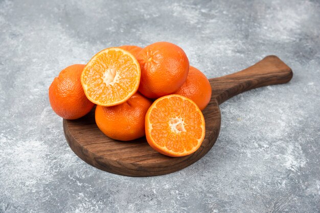 A wooden board full of juicy orange fruits with slices on stone table .