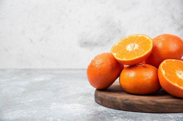 A wooden board full of juicy orange fruits with slices on stone table .