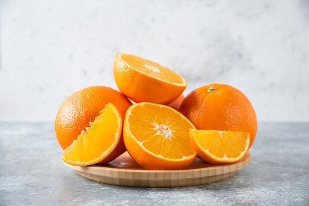 A wooden board full of juicy slices of orange fruit on stone table .