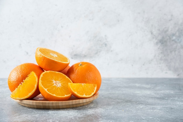 A wooden board full of juicy slices of orange fruit on stone table .