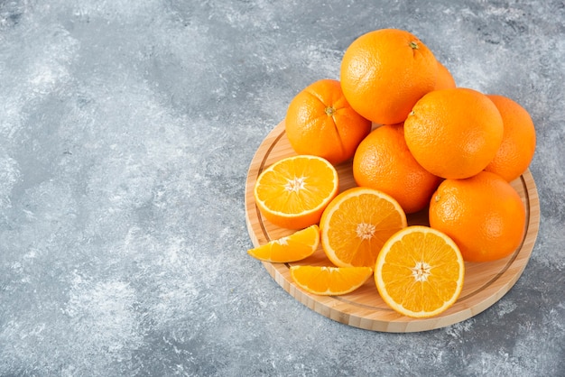 A wooden board full of juicy slices of orange fruit on stone table .