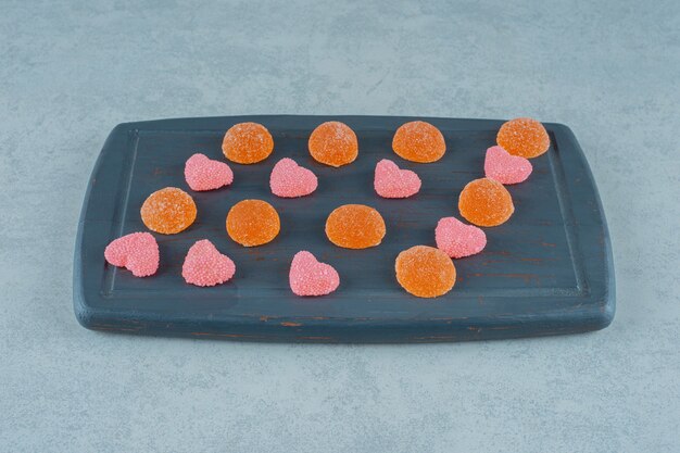 A wooden board full of orange sugary jelly candies with heart shaped jelly sweets