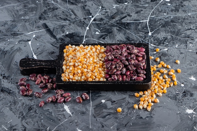 Free photo wooden board full of raw corns and beans on marble background.