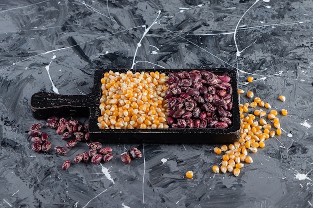 Wooden board full of raw corns and beans on marble background. 