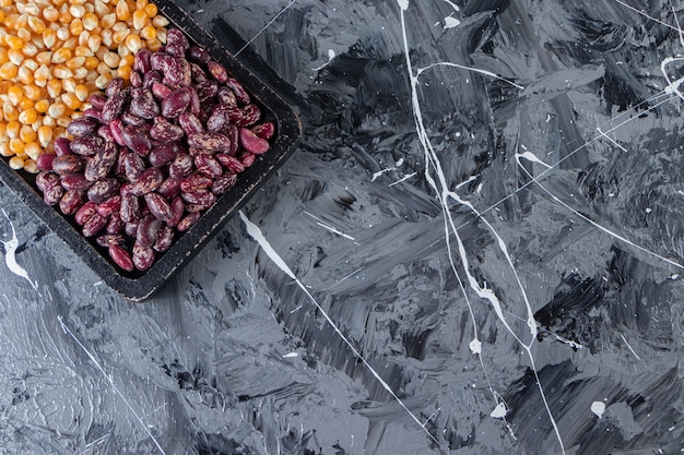 Wooden board full of raw corns and beans on marble background. 