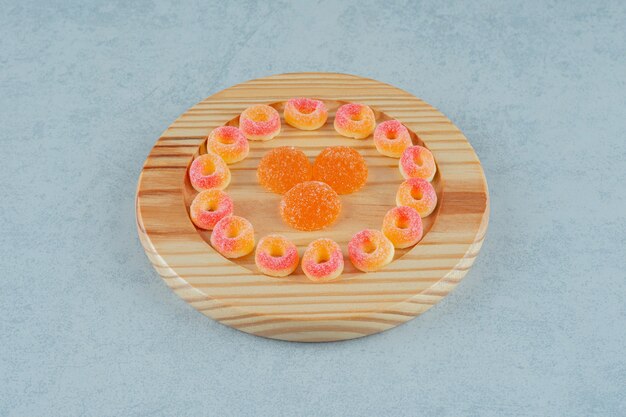 Деревянная доска, полная круглых апельсиновых желейных конфет в форме колец и апельсиновых желейных конфет с сахаром