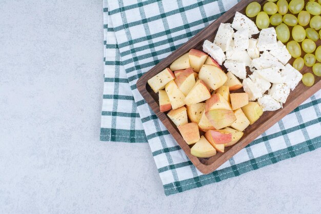 A wooden board full of white cheese and sliced fruits.