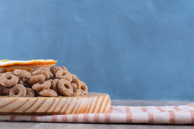 A wooden board of healthy chocolate cereal rings with a slice of orange fruit.