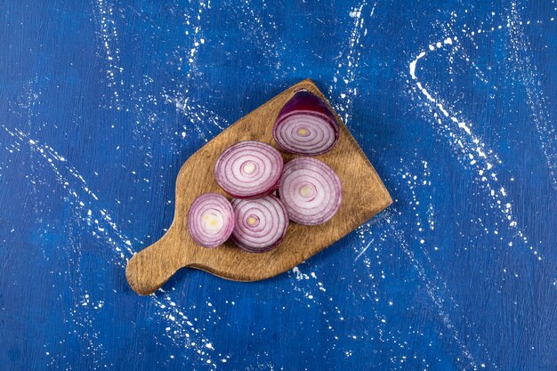 Wooden board of purple onion rings on marble table.