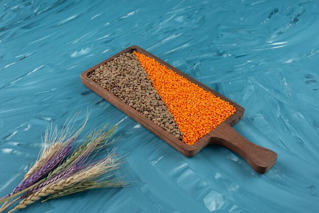 Wooden board of raw dry buckwheat and lentil on blue surface.