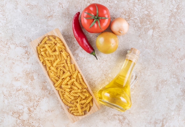 Una tavola di legno di maccheroni a spirale crudi e una bottiglia di olio di vetro