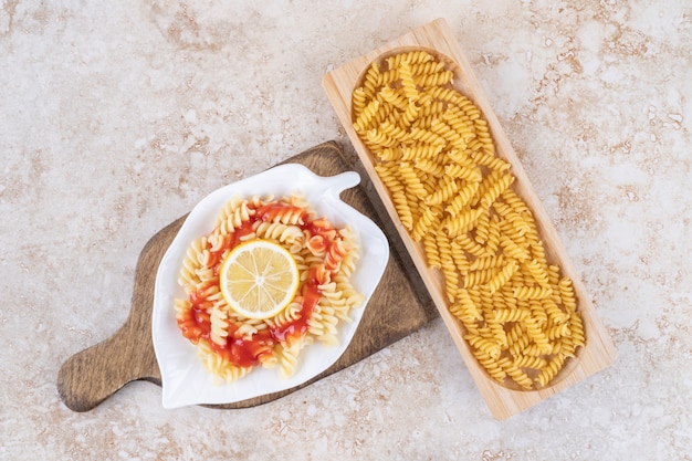 A wooden board of raw spiral macaroni and vegetables