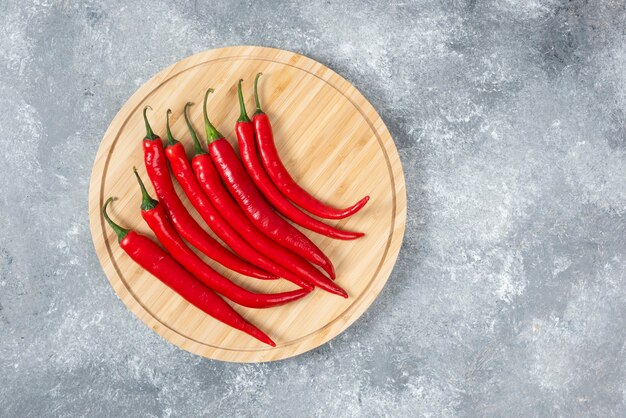 Wooden board of red chili peppers on marble surface.