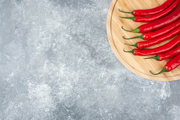 Free photo wooden board of red chili peppers on marble surface.