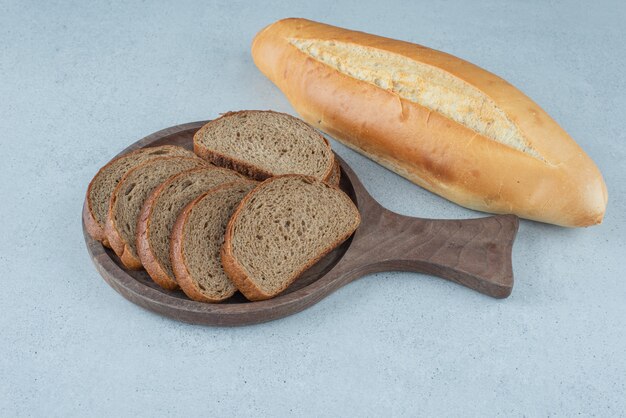 Wooden board of rye bread and bread roll on stone surface