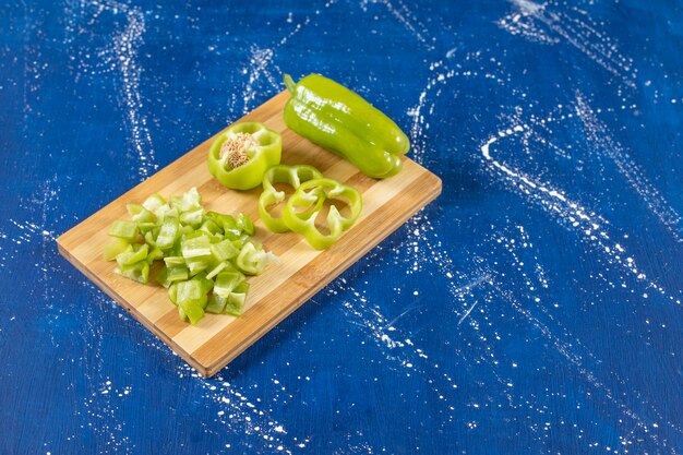 Wooden board of sliced green bell peppers on marble surface. 