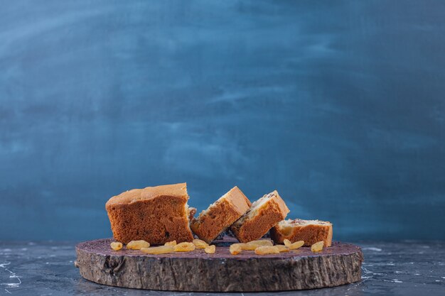 Wooden board of sliced raisin cakes on marble surface. 