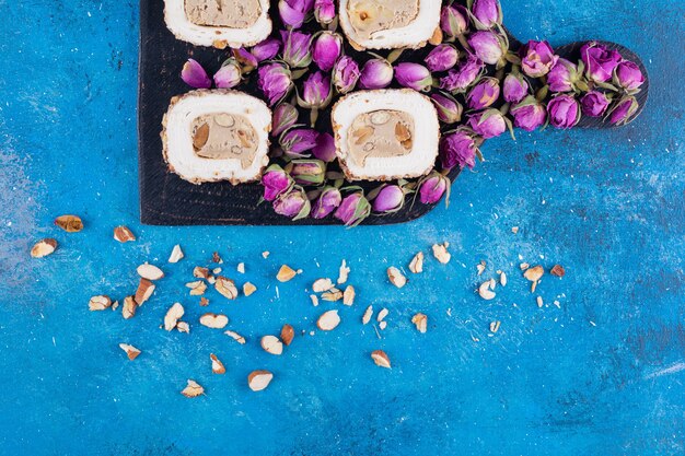 Wooden board of sweet delights and dried roses on blue table.