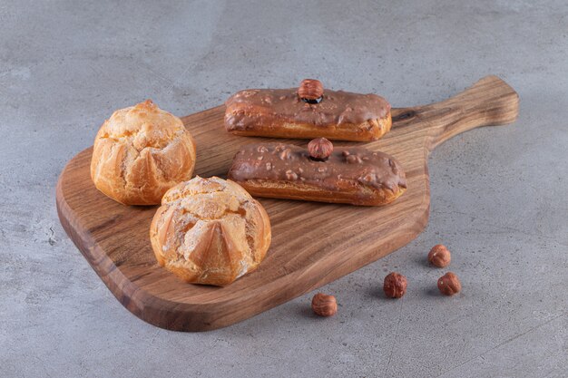 Wooden board of sweet profiteroles and eclairs on stone surface