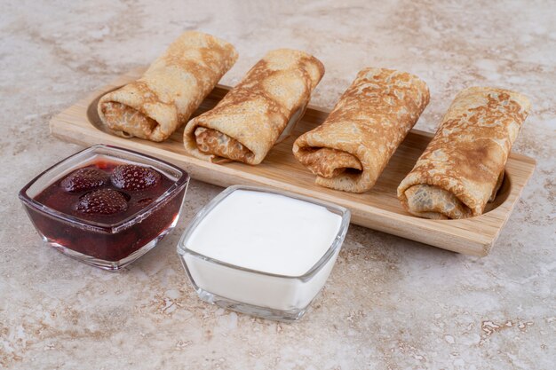 A wooden board of tasty crepes and strawberry jam 