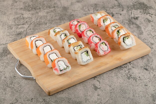 Wooden board of various sushi rolls on marble table