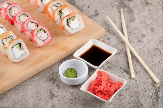 Wooden board of various sushi rolls with ginger and soy sauce on marble table