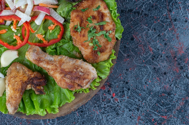 A wooden board with baked chicken meat and vegetables .