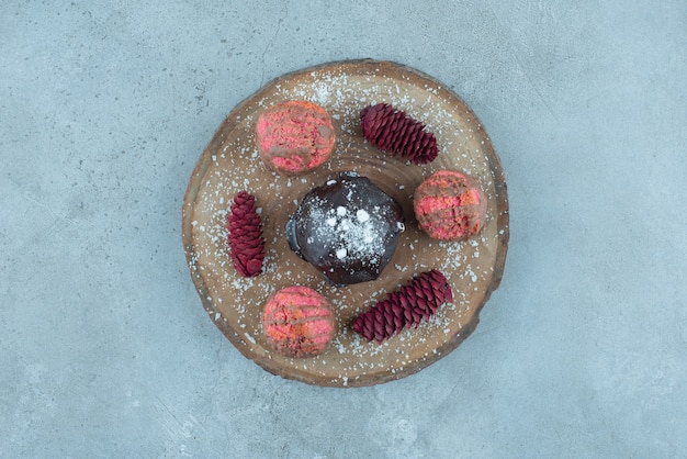 Free photo wooden board with a cake, cookies and pine cones on marble.