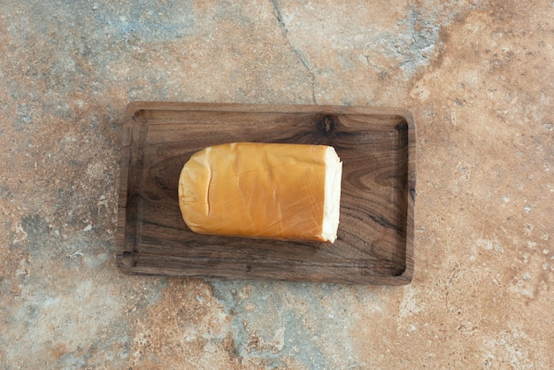 A wooden board with cheese on marble table.