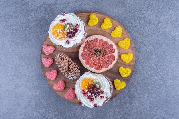 A wooden board with creamy pastries and sugary jelly candies