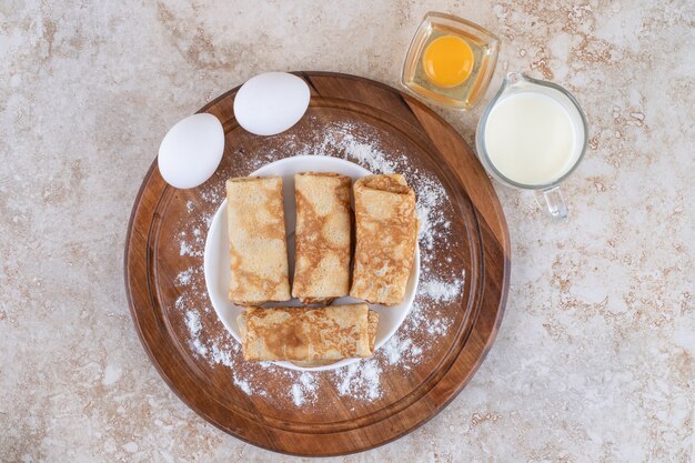 A wooden board with delicious crepes and raw eggs