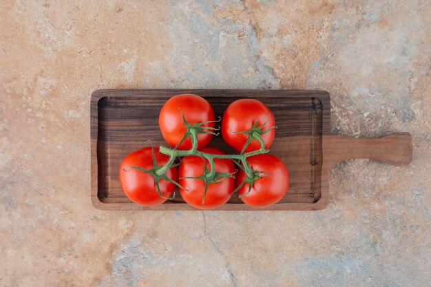 A wooden board with fresh tomatoes on marble