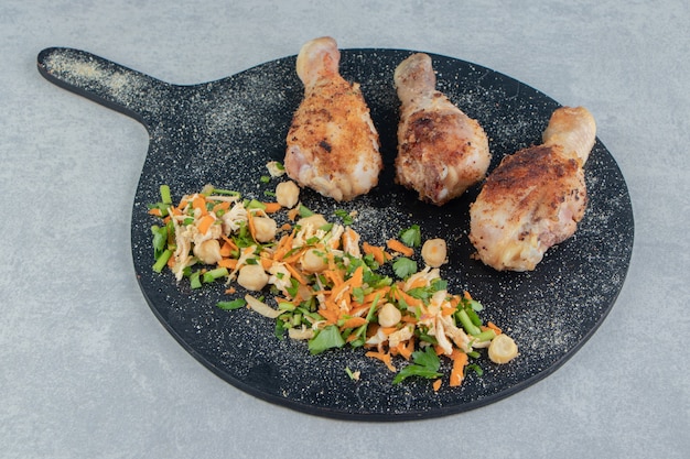 A wooden board with fried chicken legs and vegetable salad . 