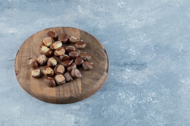 Free photo a wooden board with healthy chestnuts on a gray background.