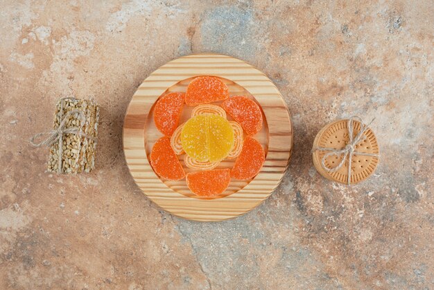 A wooden board with marmalade and cookies on marble background