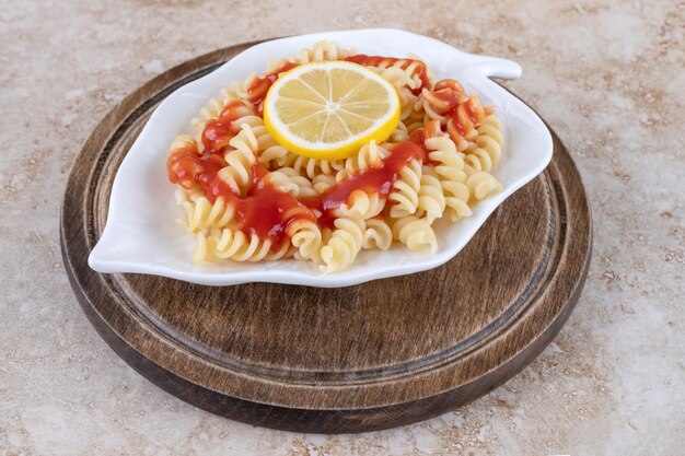 Wooden board with a platter of lemon-topped pasta on marble surface