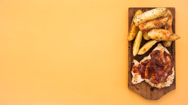 Wooden board with potato wedges and grilled meat