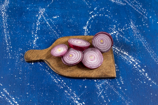 Wooden board with purple onion rings on marble surface