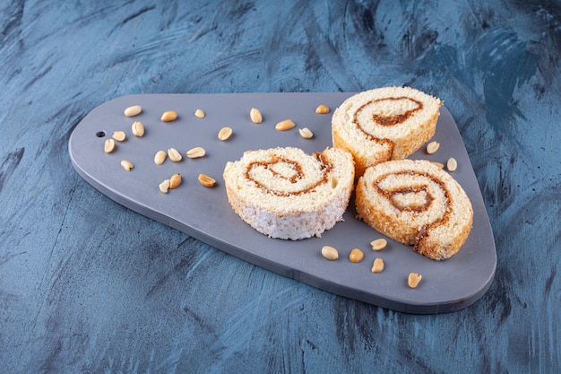 Free photo wooden board with sliced roll cake and peanuts on blue.