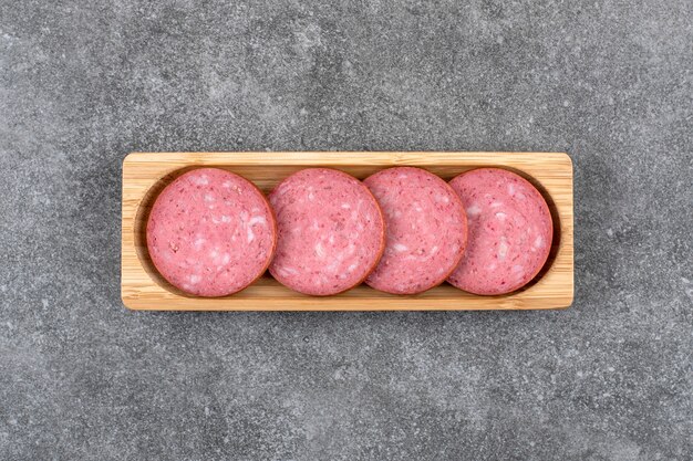 Wooden board with sliced salami placed on stone table. 