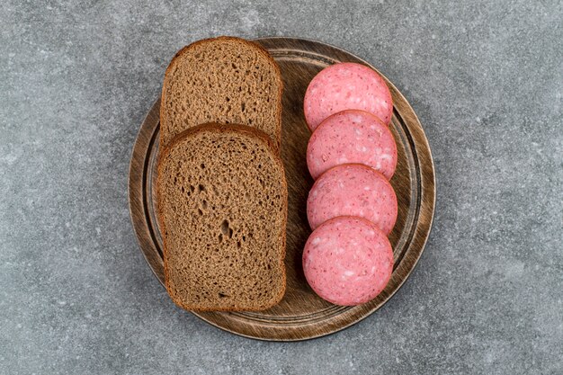 Wooden board with sliced salami placed on stone table. 