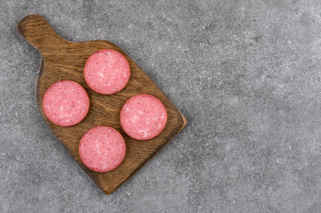 Wooden board with sliced salami placed on stone table. 