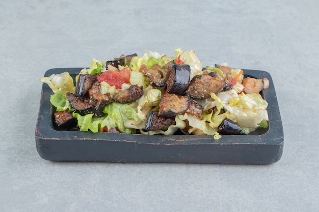 A wooden board with vegetable salad and fried eggplant . 