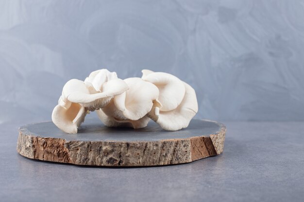 A wooden board with white mushrooms . 