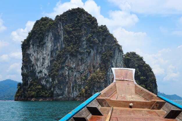 Wooden boat on the sea surrounded by rock formations under a blue cloudy sky