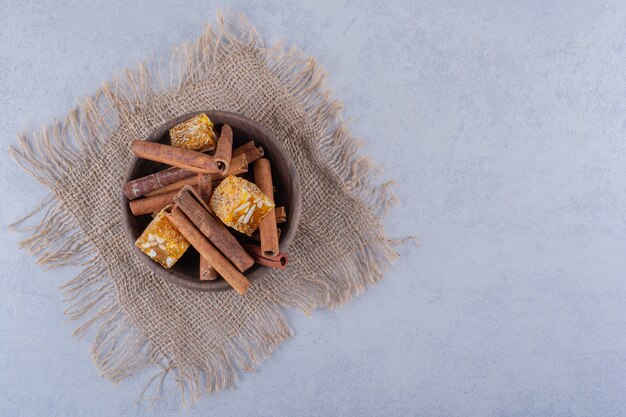 Wooden bowl of cinnamon sticks and nut candies on stone table. 