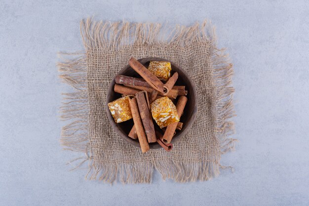 Wooden bowl of cinnamon sticks and nut candies on stone table. 