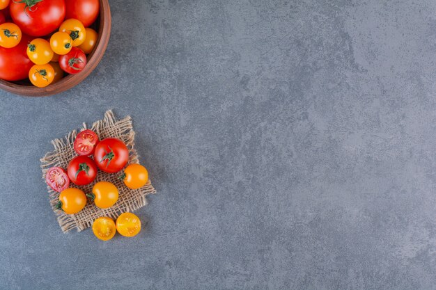 Wooden bowl of colorful organic tomatoes on stone surface